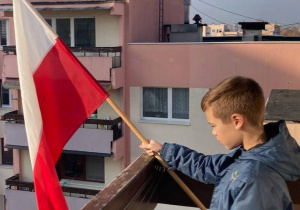 Chłopiec stoi na balkonie i trzyma flagę biało-czerwoną.